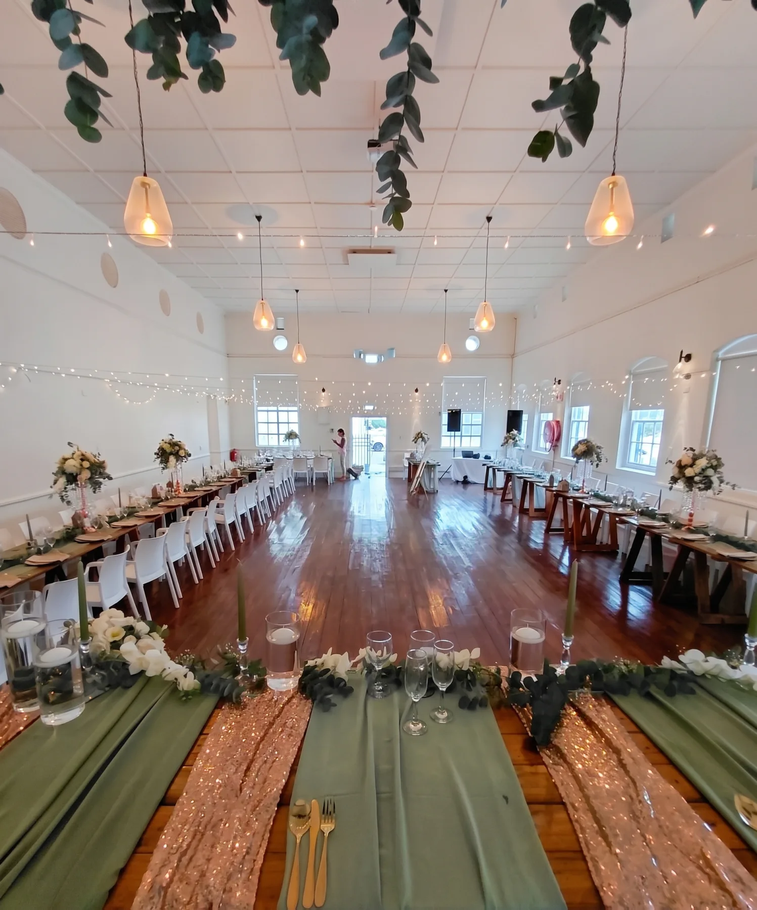 Long banquet tables running the length of a hall, sage runners and pendant lights overhead